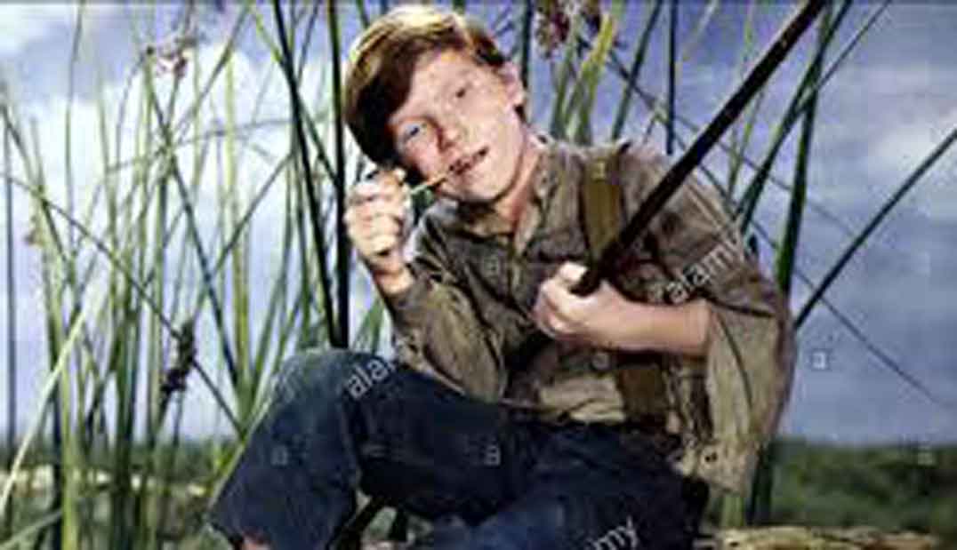 fotograma de película de los años 50 sobre Huckeberry Finn, niño protagonista fumando pipa y con una caña, color
